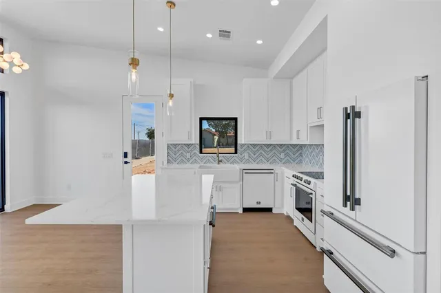 a view of a kitchen with a sink and dishwasher a refrigerator with white cabinets