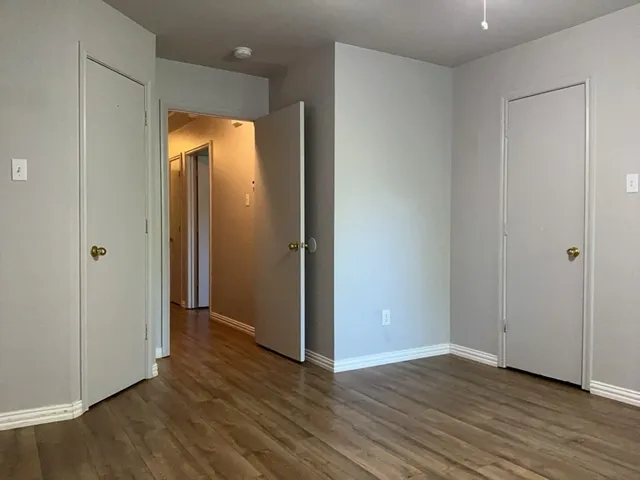 a view of an empty room with wooden floor and a bathroom