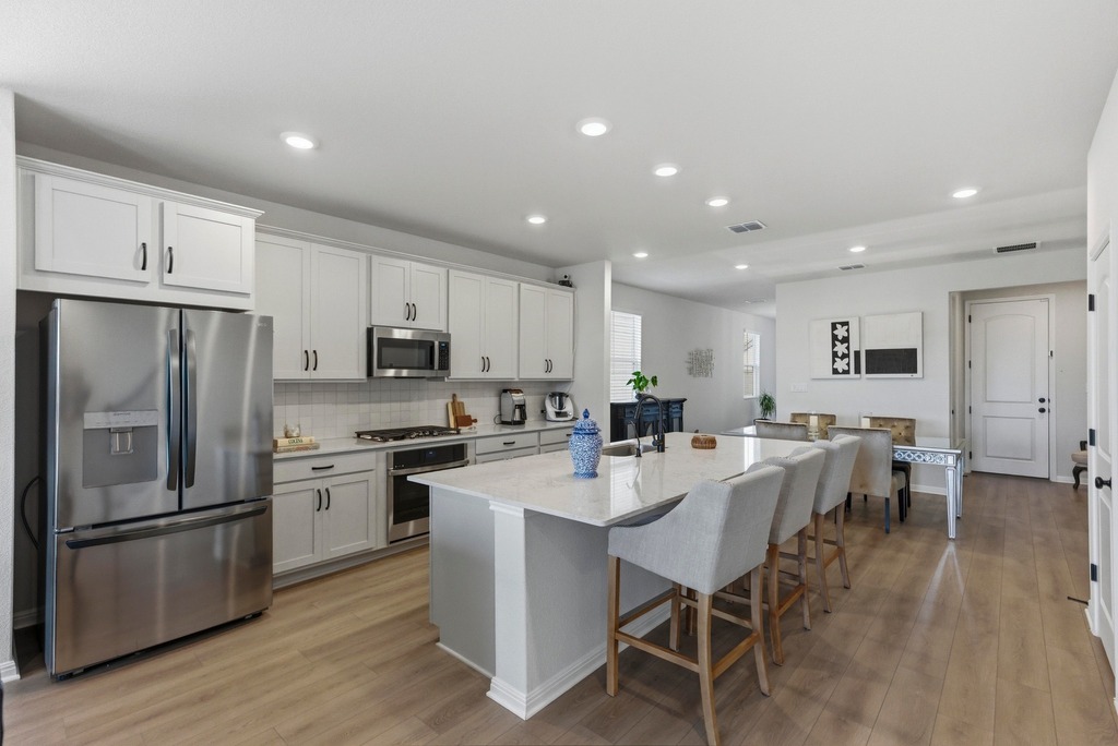 264 Denali Way Dripping Springs, TX 78620 - Photo 5 of 28 Kitchen featuring appliances with stainless steel finishes, light stone countertops, a breakfast bar area, light wood-style flooring, and an island with sink