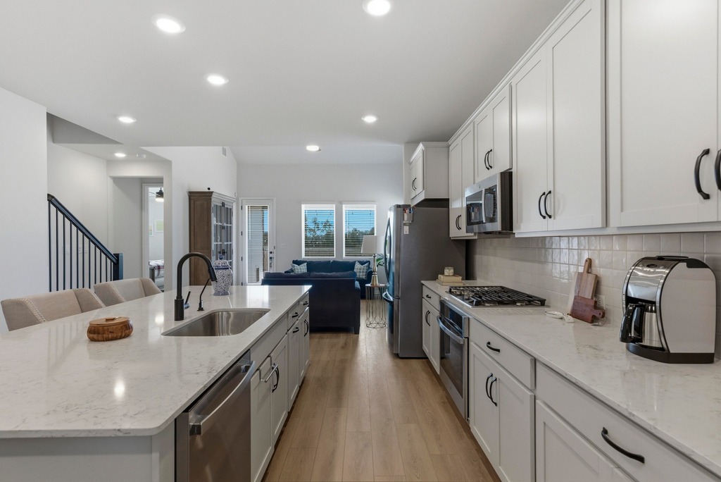 264 Denali Way Dripping Springs, TX 78620 - Photo 27 of 28 Kitchen with light stone counters, a kitchen island with sink, appliances with stainless steel finishes, open floor plan, and white cabinetry