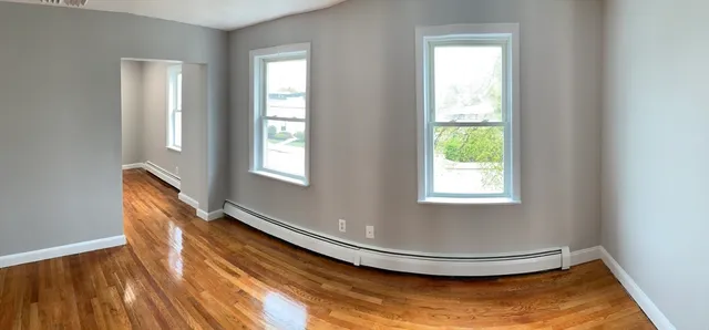 a view of an empty room with wooden floor and a window