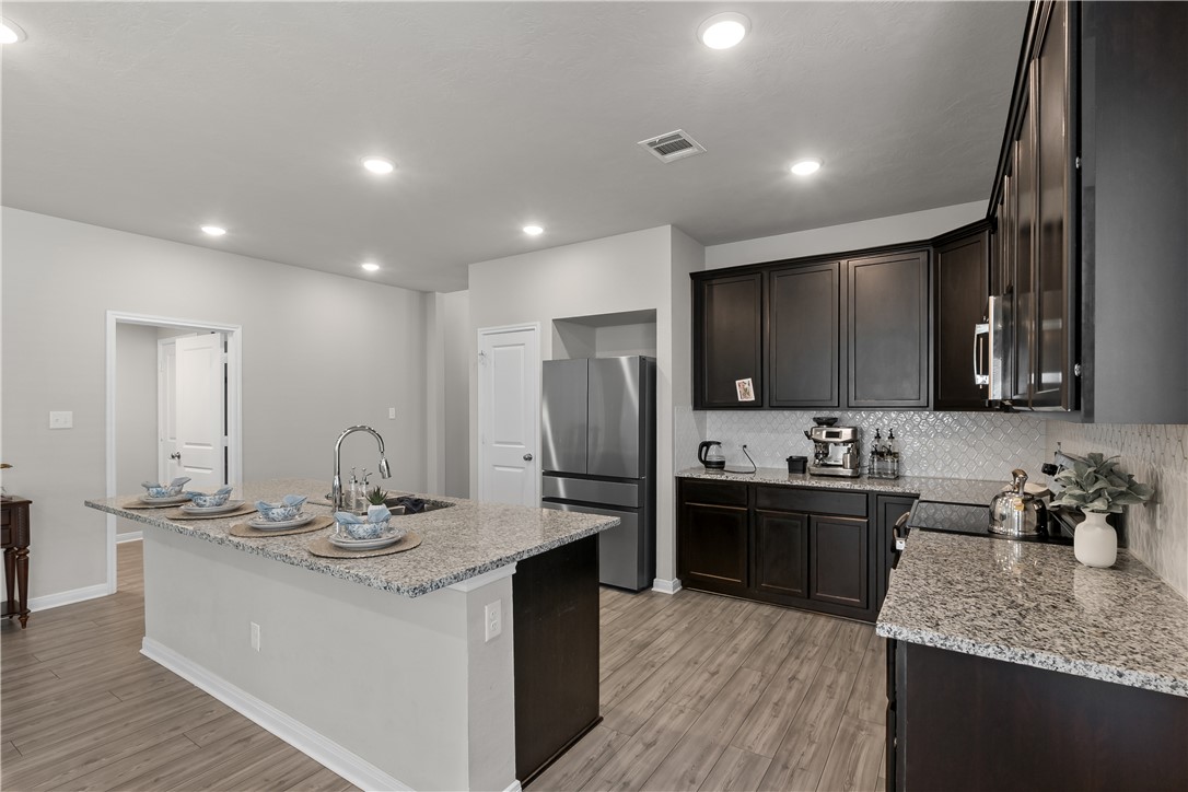 1925 Viva Road Bryan, TX 77807 - Photo 5 of 25 Kitchen featuring light stone countertops, freestanding refrigerator, a center island with sink, backsplash, and light wood finished floors