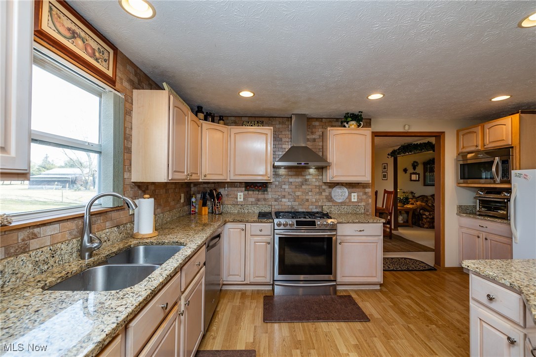 12181 Williams Road Homerville, OH 44235 - Photo 6 of 49 Kitchen featuring appliances with stainless steel finishes, a textured ceiling, light hardwood / wood-style flooring, wall chimney exhaust hood, and sink