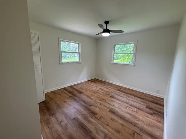 an empty room with wooden floor ceiling fan and windows
