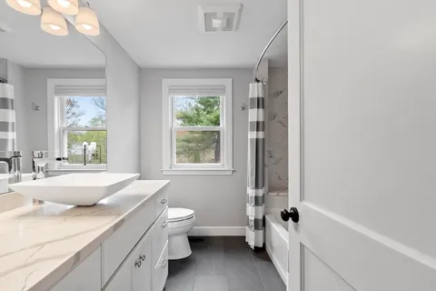 a bathroom with a granite countertop sink a large mirror a bathtub and next to a window