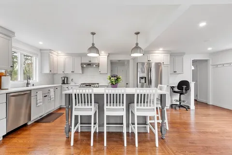 a kitchen with stainless steel appliances granite countertop a dining table chairs stove and white cabinets