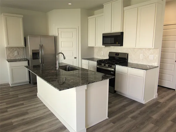 a kitchen with granite countertop a stove top oven a sink a counter space and cabinets