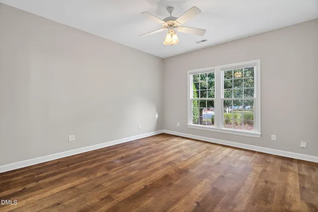 a view of an empty room with chandelier fan and wooden floor