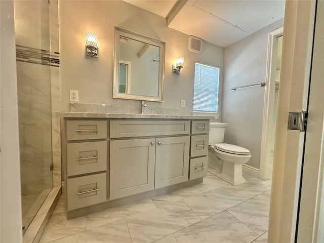 a spacious bathroom with a granite countertop sink toilet a mirror and shower