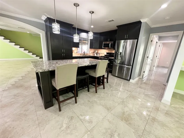 a kitchen with stainless steel appliances kitchen island granite countertop dining table chairs and a refrigerator