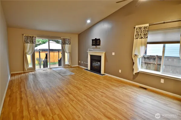 a big room with wooden floor a fireplace and windows