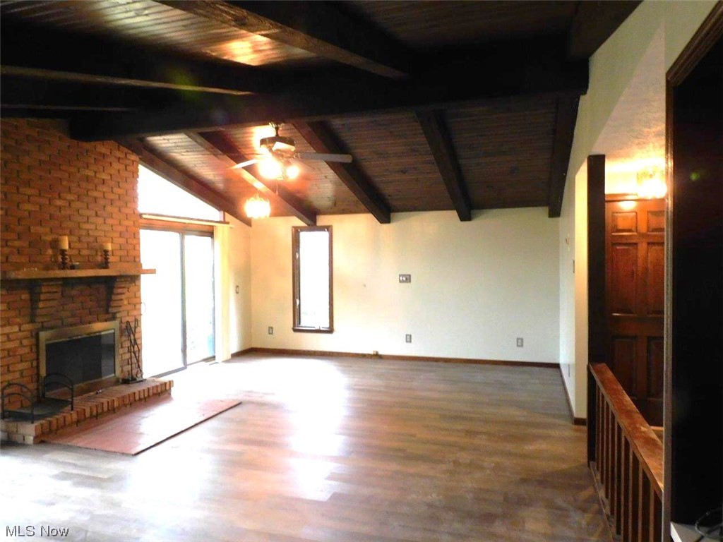 1102 Fiesta Road Southwest Dellroy, OH 44620 - Photo 7 of 20 Unfurnished living room with a brick fireplace, brick wall, lofted ceiling with beams, dark wood-type flooring, and ceiling fan