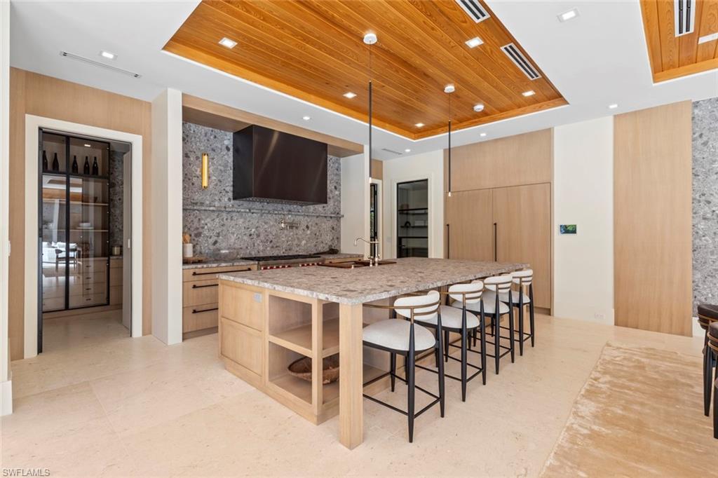 508 16th Avenue South Naples, FL 34102 - Photo 13 of 50 Kitchen with a raised ceiling, light brown cabinets, wooden ceiling, light stone counters, and a kitchen breakfast bar