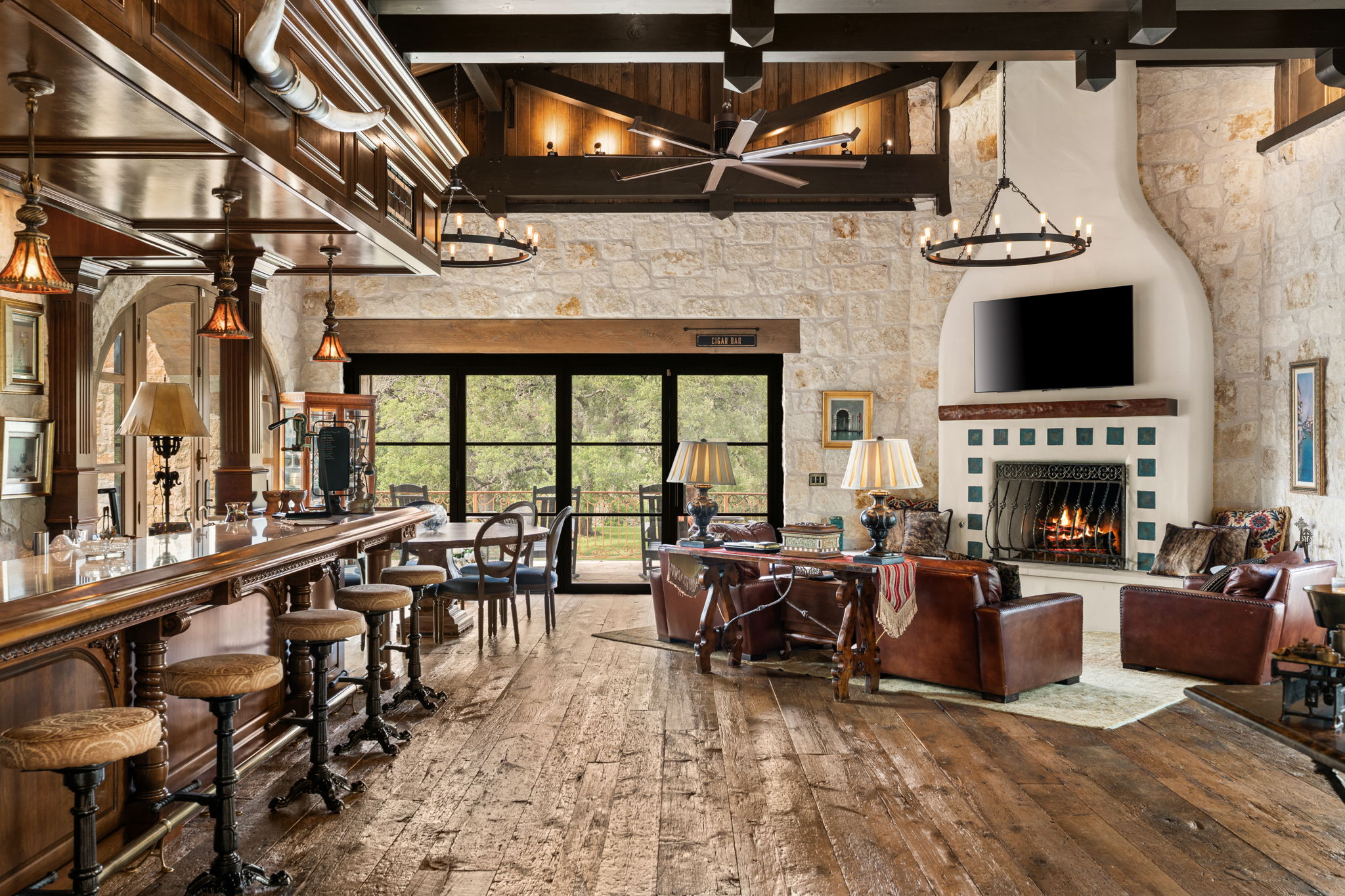 11941 Overlook Pass Austin, TX 78738 - Photo 36 of 40 Great room featuring an ornate wood bar with stools, a stone fireplace with tiled hearth, wood-finish flooring, exposed wood beam ceiling, and expansive glass doors