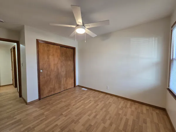 an empty room with wooden floor closet and fan