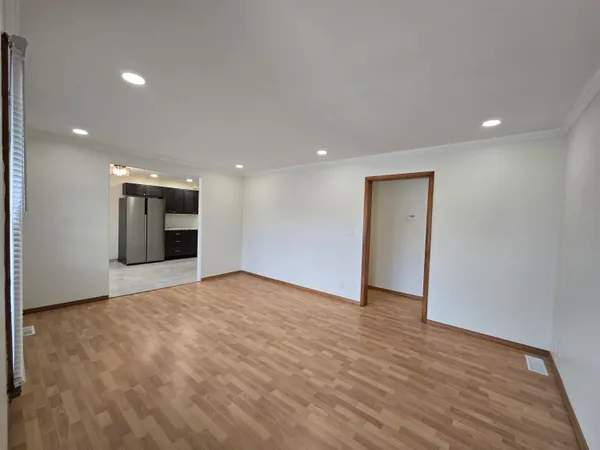 a view of an empty room with wooden floor and kitchen