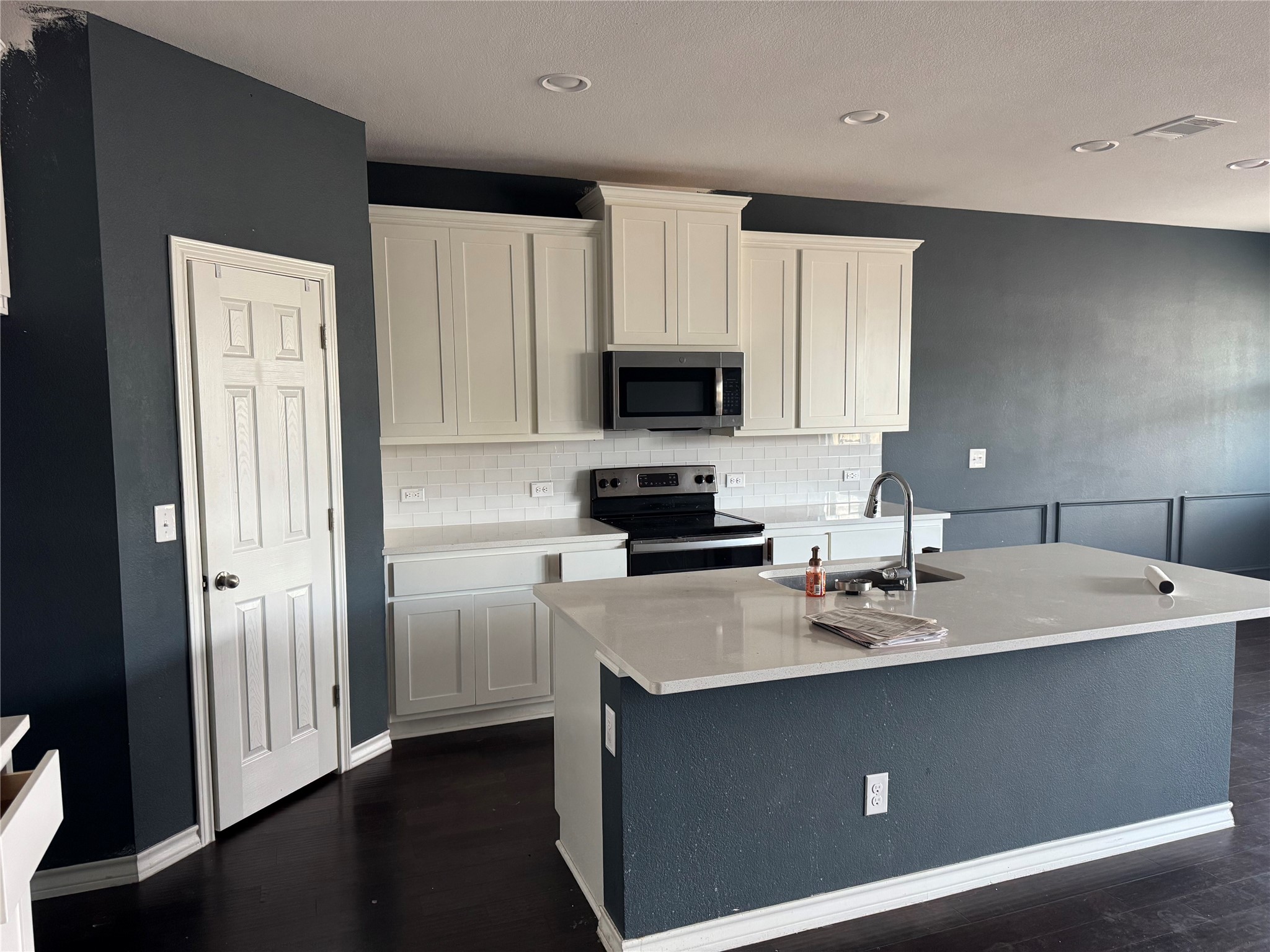 333 Capstone Road Liberty Hill, TX 78642 - Photo 11 of 40 Two tone kitchen featuring stainless steel appliances, tasteful backsplash, a kitchen island with sink, dark wood-type flooring, and light stone counters
