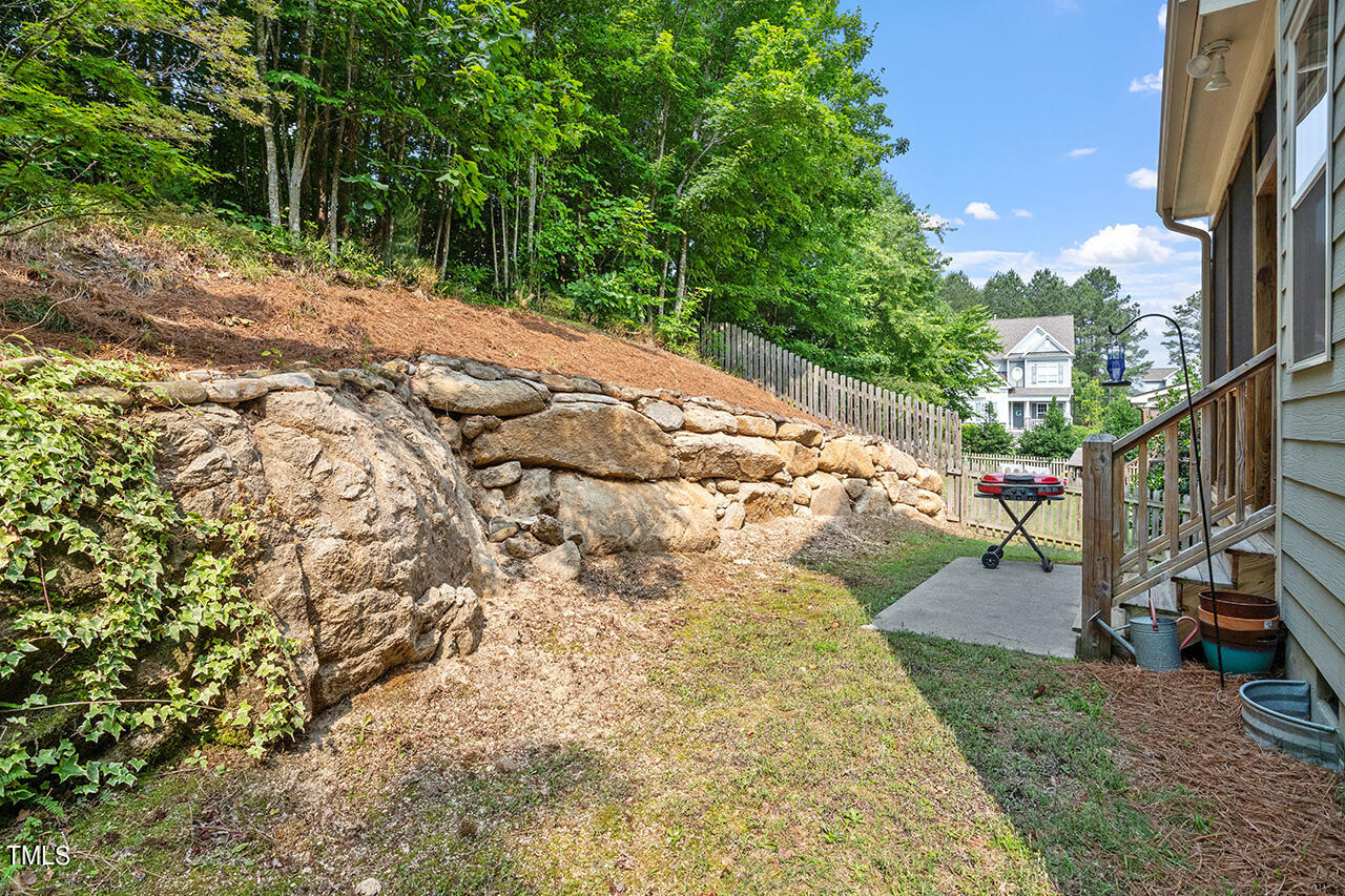 3051 Freeman Farm Way Rolesville, NC 27571 - Photo 33 of 37 The private back yard extends beyond the natural rock wall to a wooded area above that can be cleared for additional use if desired