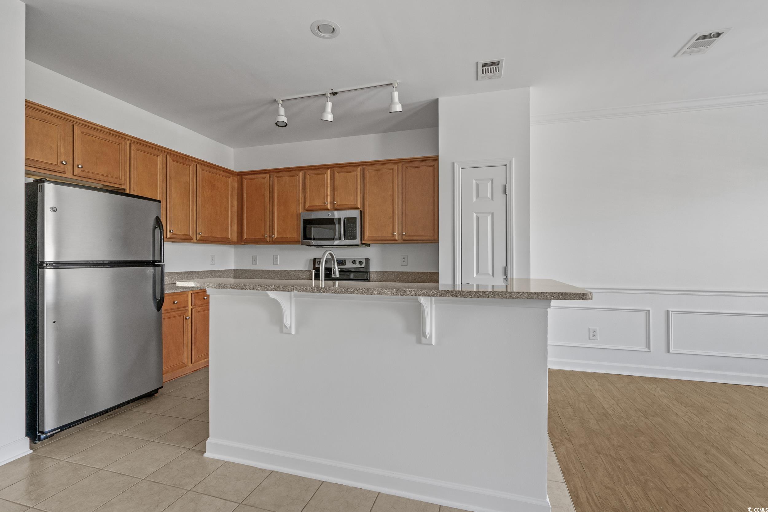 2798 Howard Avenue, Unit B Myrtle Beach, SC 29577 - Photo 11 of 40 Kitchen with appliances with stainless steel finishes, a breakfast bar area, a decorative wall, light stone counters, and rail lighting