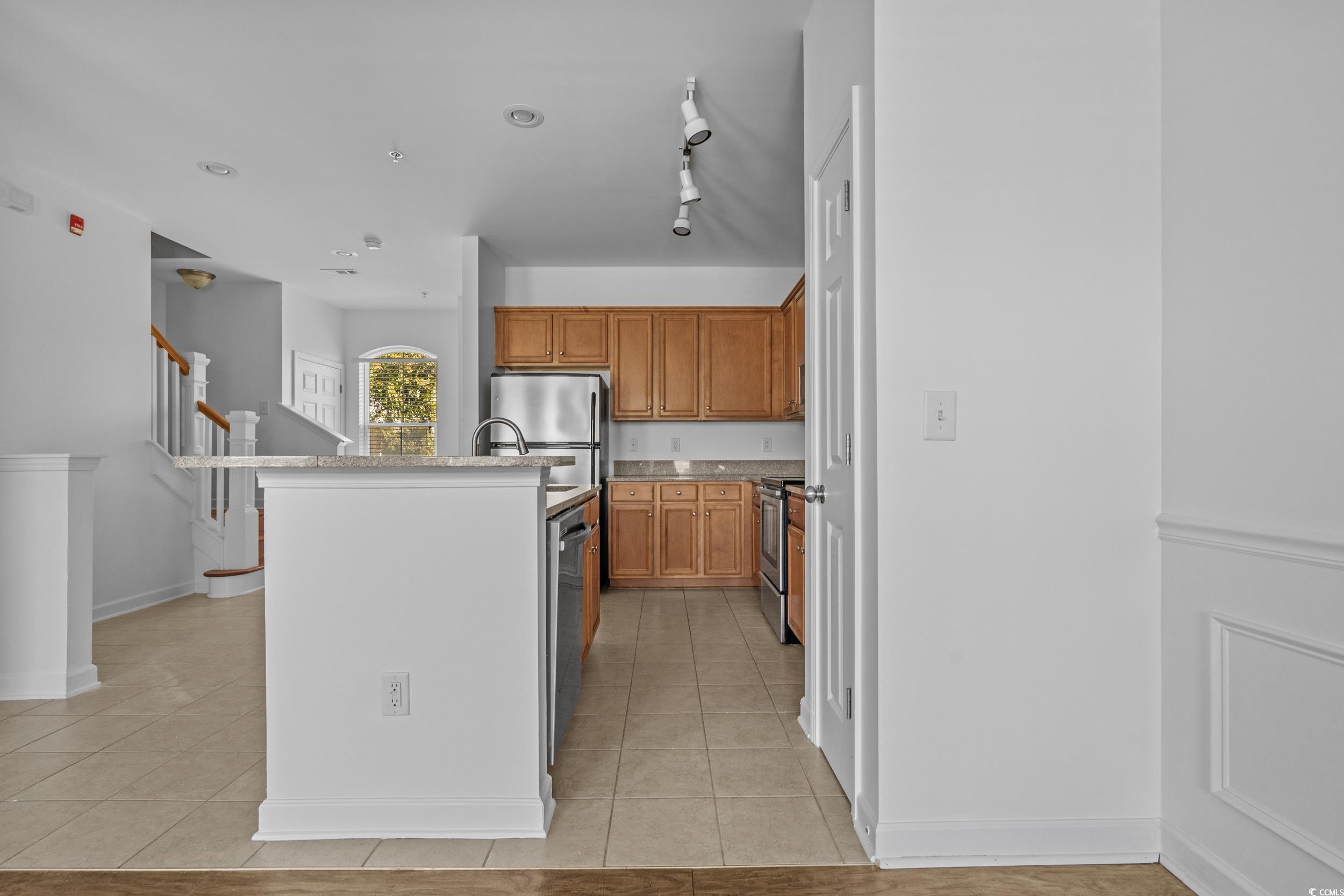 2798 Howard Avenue, Unit B Myrtle Beach, SC 29577 - Photo 12 of 40 Kitchen featuring light tile patterned flooring, an island with sink, brown cabinetry, stainless steel appliances, and light stone countertops
