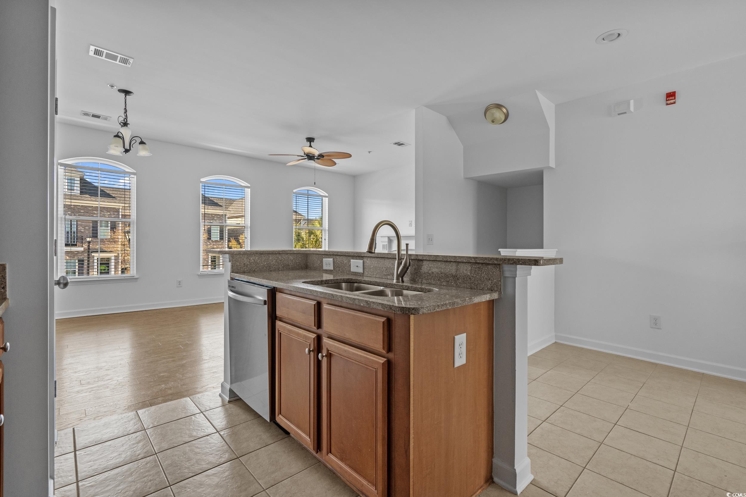 2798 Howard Avenue, Unit B Myrtle Beach, SC 29577 - Photo 13 of 40 Kitchen with brown cabinetry, an island with sink, dark stone counters, light tile patterned floors, and stainless steel dishwasher