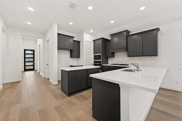 a large kitchen with stainless steel appliances a sink dishwasher a refrigerator and a stove with wooden floor