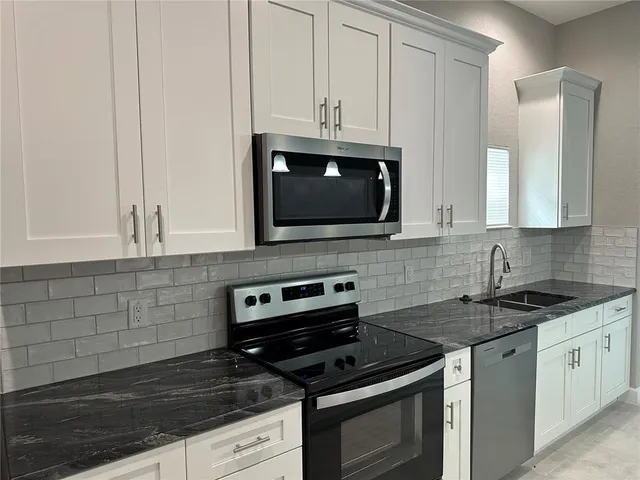 a kitchen with stainless steel appliances granite countertop white cabinets a sink and a white stove