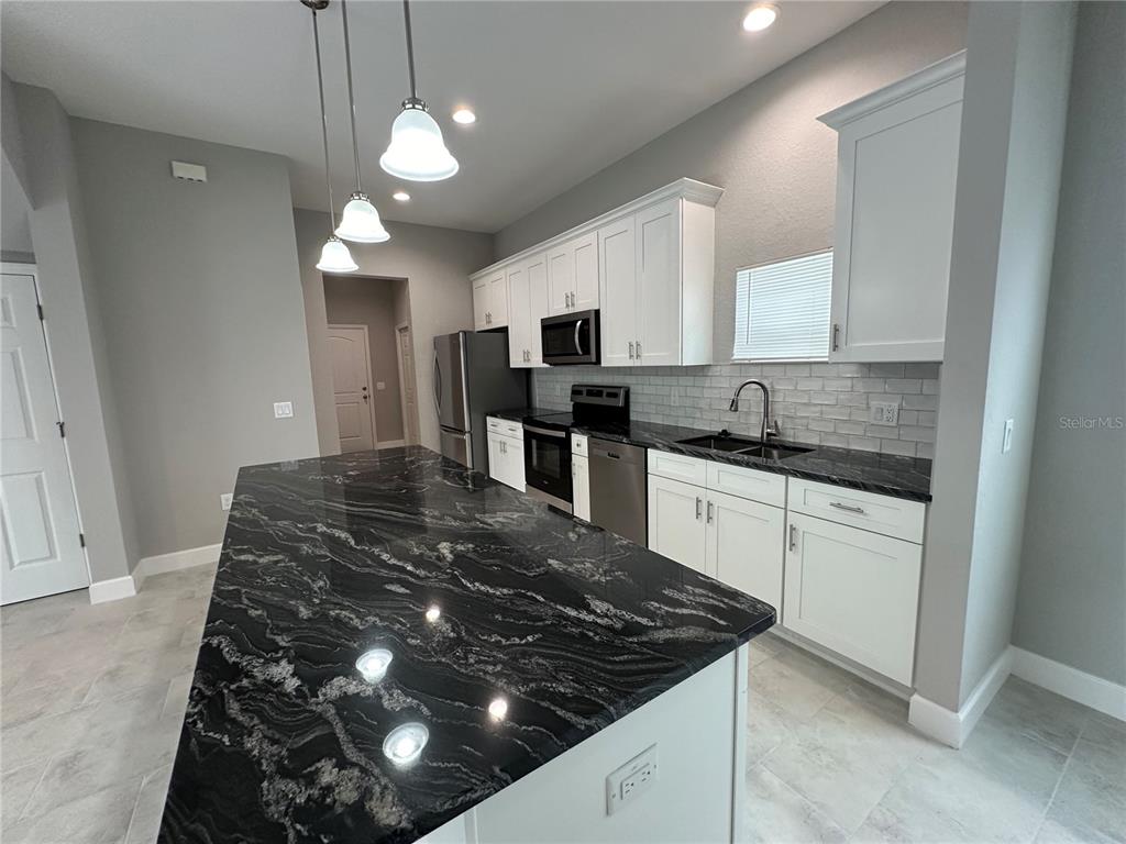 4920 8th Street Zephyrhills, FL 33542 - Photo 15 of 57 a kitchen with kitchen island granite countertop a stove top oven a sink a counter space and cabinets
