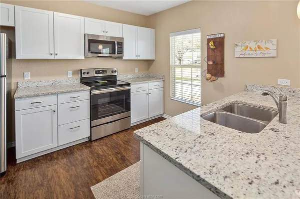 a kitchen with granite countertop a sink a stove and cabinets