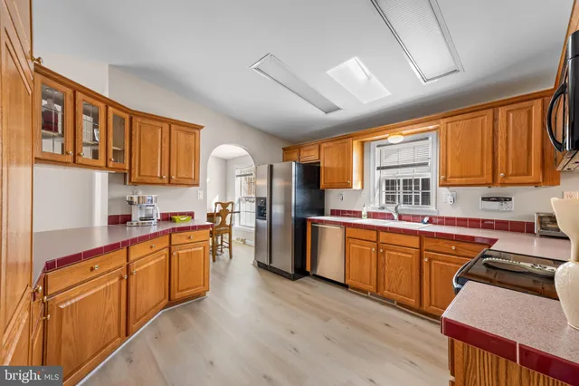 a kitchen with stainless steel appliances granite countertop wooden cabinets a refrigerator a sink a stove and wooden floors