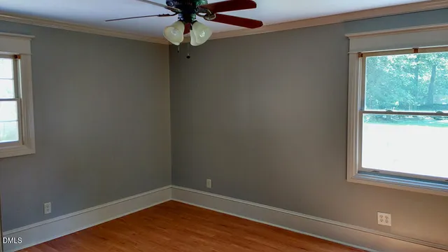 an empty room with wooden floor fan and windows
