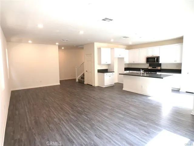 a kitchen with stainless steel appliances a stove top oven a sink and white cabinets with wooden floor