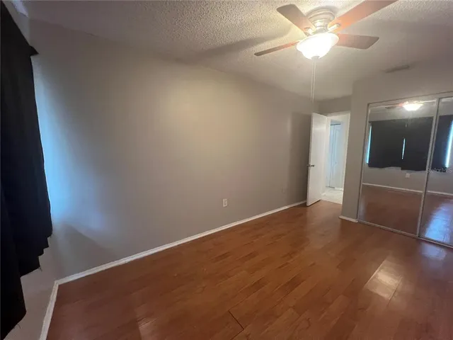 an empty room with wooden floor and way to kitchen