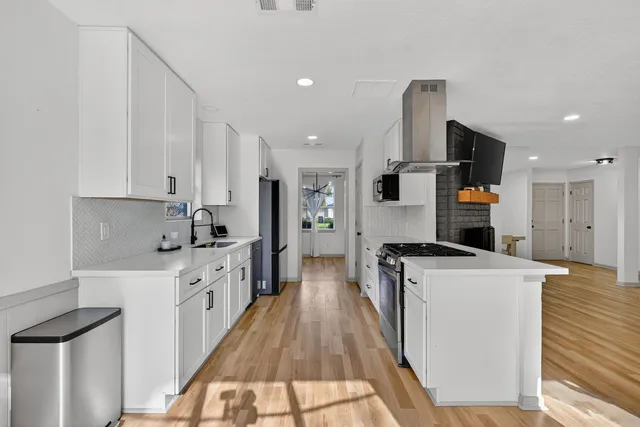 a large kitchen with stainless steel appliances kitchen island a stove a refrigerator a oven and white cabinets with wooden floor