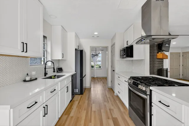 a kitchen with stainless steel appliances a sink stove oven a refrigerator white cabinets and wooden floor