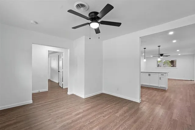 a view of an empty room with wooden floor and a ceiling fan