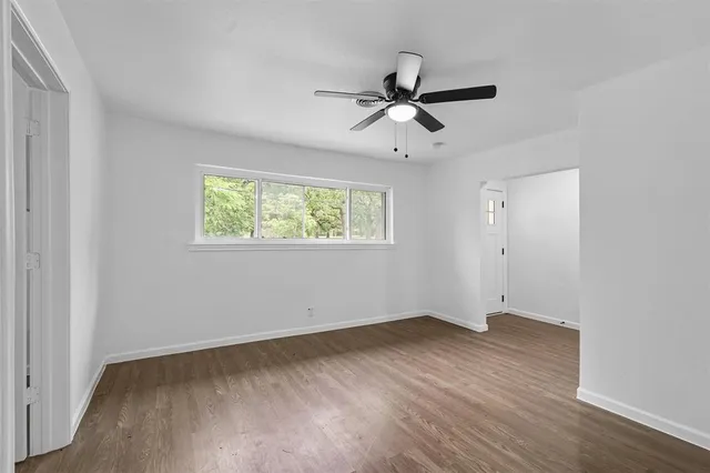 an empty room with wooden floor fan and windows