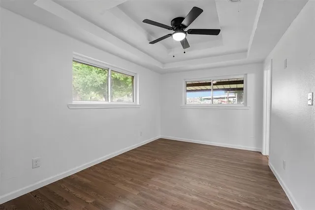 an empty room with wooden floor ceiling fan and windows
