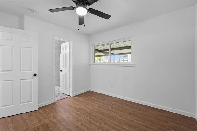 an empty room with wooden floor ceiling fan and windows