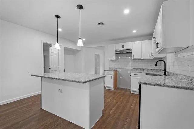 a kitchen with stainless steel appliances granite countertop a sink a stove a refrigerator and white cabinets with wooden floor