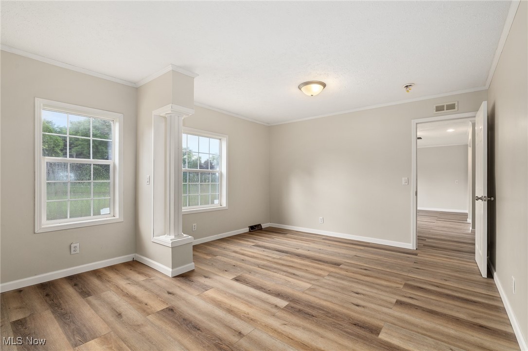 4838 Angling Rd Extension Wooster, OH 44691 - Photo 17 of 39 Spare room with crown molding, light wood-style flooring, decorative columns, and a pendent fire sprinkler