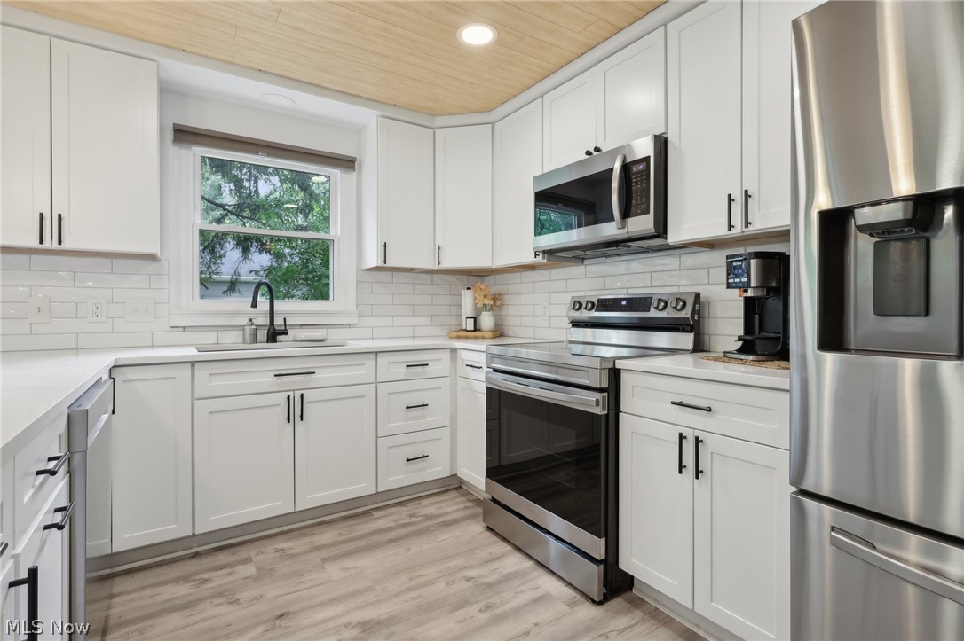 139 Solon Road Chagrin Falls, OH 44022 - Photo 11 of 41 Kitchen featuring white cabinetry, tasteful backsplash, light hardwood / wood-style floors, appliances with stainless steel finishes, and sink