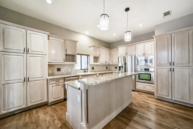 a kitchen with stainless steel appliances granite countertop a refrigerator a sink dishwasher a stove and white cabinets with wooden floor