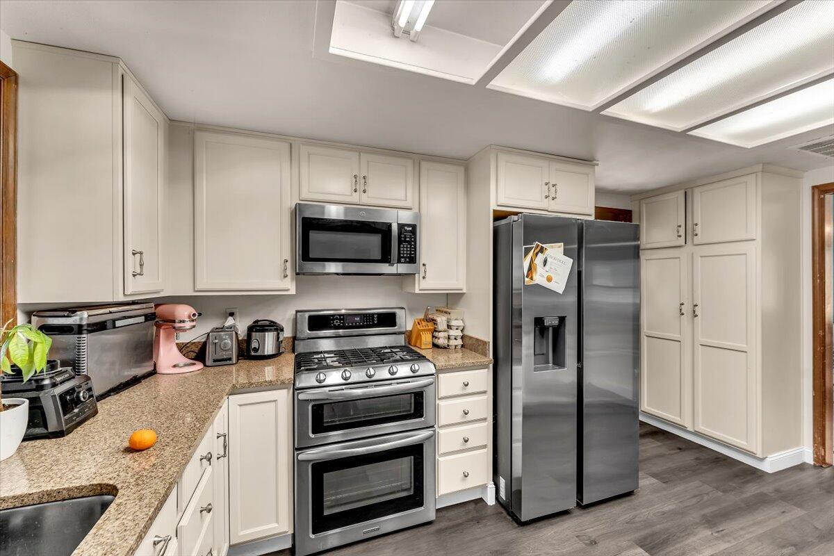 13160 Bear Mountain Road Redding, CA 96003 - Photo 27 of 40 a kitchen with refrigerator a microwave a stove and white cabinets with wooden floor