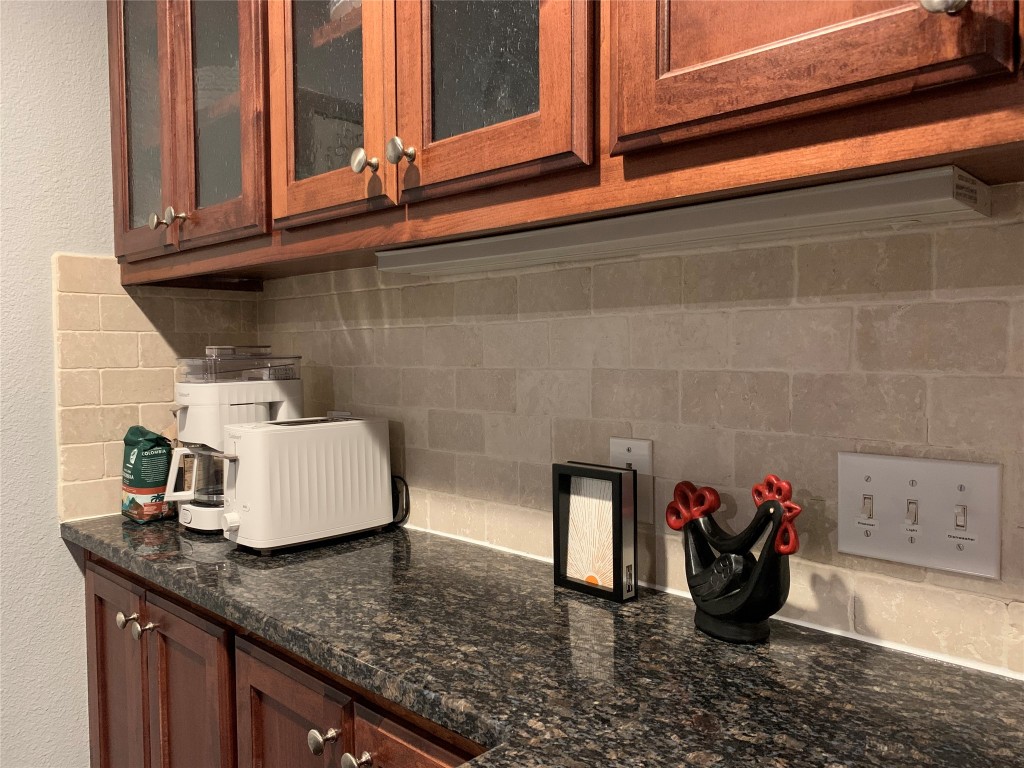 407 East 45th Street, Unit 116 Austin, TX 78751 - Photo 7 of 19 Kitchen view of dark stone countertops, decorative backsplash, glass insert cabinets, a textured wall, and brown cabinetry
