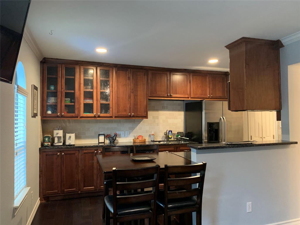 407 East 45th Street, Unit 116 Austin, TX 78751 - Photo 8 of 19 Kitchen with dark stone counters, stainless steel refrigerator with ice dispenser, crown molding, glass insert cabinets, and dark wood finished floors