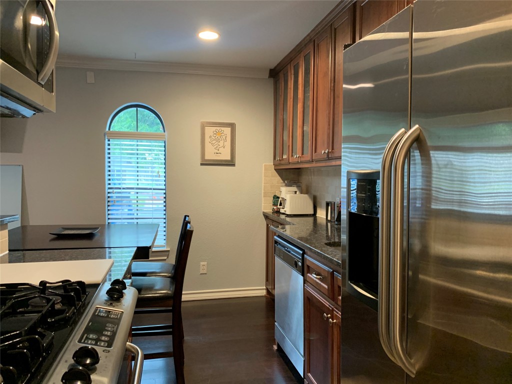 407 East 45th Street, Unit 116 Austin, TX 78751 - Photo 9 of 19 Kitchen with stainless steel appliances, glass insert cabinets, crown molding, dark stone countertops, and dark wood-style flooring