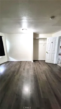 a view of an empty room with wooden floor and kitchen