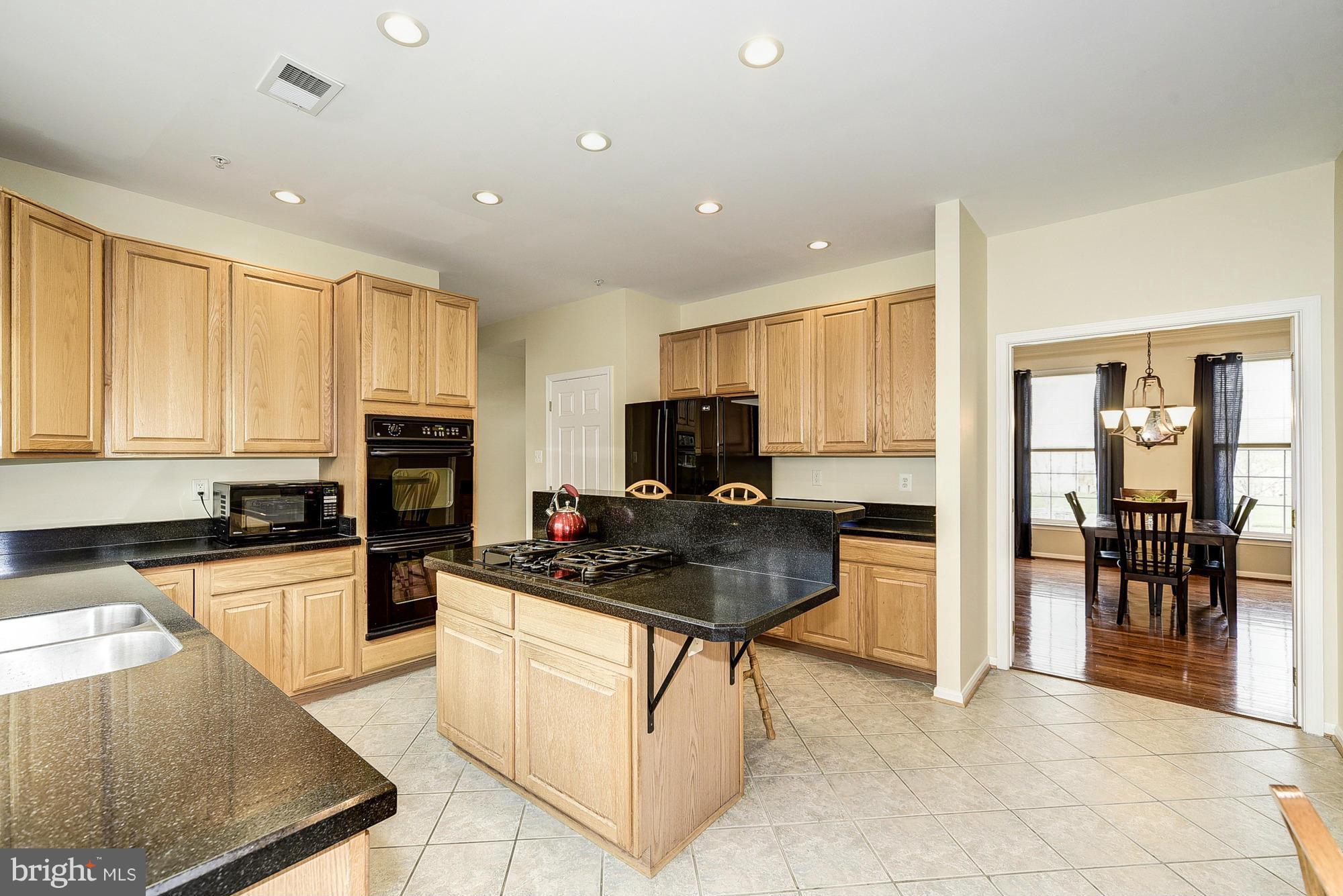 11204 Snowden Pond Road Laurel, MD 20708 - Photo 8 of 30 a kitchen with stainless steel appliances granite countertop a stove top oven a sink a dining table and chairs with wooden floor