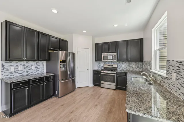 a kitchen with stainless steel appliances granite countertop a stove a sink dishwasher a refrigerator and a microwave oven with wooden floor